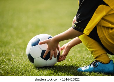 Child playing with soccer ball on grass venue. Little kid holding in both hands football ball. Young soccer player in blue cleats - Powered by Shutterstock