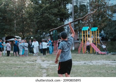 The Child Playing With Stick In Nature. Boy Imagines Himself A Mammoth Hunter And Running With Stick On People.