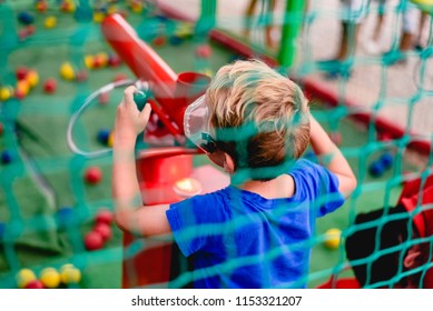 Child Playing At A Summer Fair With A Cannon Of Colored Balls Of Compressed Air.