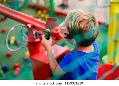 Child Playing At A Summer Fair With A Cannon Of Colored Balls Of Compressed Air.