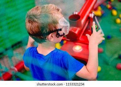 Child Playing At A Summer Fair With A Cannon Of Colored Balls Of Compressed Air.