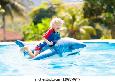 Child playing in swimming pool. Kids learn to swim. Little baby with inflatable toy float playing in water on summer vacation in tropical resort. Kid with toy shark on beach holiday.