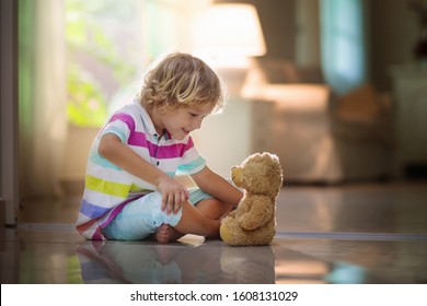 Child Playing With Teddy Bear. Little Boy Hugging His Favorite Toy. Kid And Stuffed Animal At Home. Toddler Sitting On The Floor Of Living Room With Big Window At Sun Set. Kids Play Indoors.