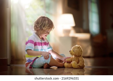 Child Playing With Teddy Bear. Little Boy Hugging His Favorite Toy. Kid And Stuffed Animal At Home. Toddler Sitting On The Floor Of Living Room With Big Window At Sun Set. Kids Play Indoors.