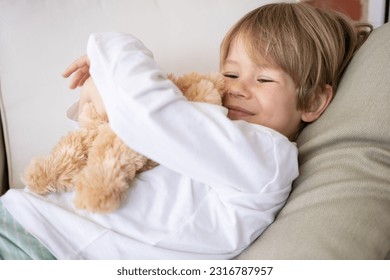Child playing with teddy bear. Little boy hugging his favorite toy. Kid and stuffed animal at home. Toddler sitting on the floor of living room. Kids play indoors.