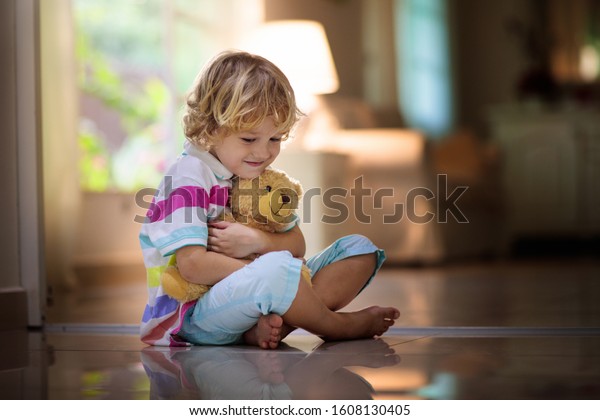 Child\
playing with teddy bear. Little boy hugging his favorite toy. Kid\
and stuffed animal at home. Toddler sitting on the floor of living\
room with big window at sun set. Kids play\
indoors.