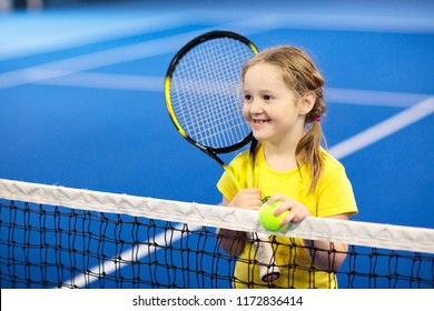 Child Playing Tennis On Indoor Court. Little Girl With Tennis Racket And Ball In Sport Club. Active Exercise For Kids. Summer Activities For Children. Training For Young Kid. Child Learning To Play.