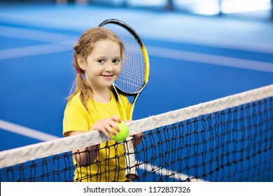 Child Playing Tennis On Indoor Court. Little Girl With Tennis Racket And Ball In Sport Club. Active Exercise For Kids. Summer Activities For Children. Training For Young Kid. Child Learning To Play.