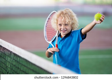 Child Playing Tennis On Indoor Court. Little Boy With Tennis Racket And Ball In Sport Club. Active Exercise For Kids. Summer Activities For Children. Training For Young Kid. Child Learning To Play.