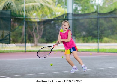 Child Playing Tennis On Indoor Court. Little Girl With Tennis Racket And Ball In Sport Club. Active Exercise For Kids. Summer Activities For Children. Training For Young Kid. Child Learning To Play.