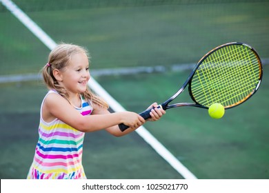 Child Playing Tennis On Outdoor Court. Little Girl With Tennis Racket And Ball In Sport Club. Active Exercise For Kids. Summer Activities For Children. Training For Young Kid. Child Learning To Play.