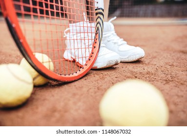 Child Playing Tennis On Outdoor Court. Cropped Image Of Child Legs On Tennis Court. Closeup Of Tennis Ball, Racket And Shoes. Active Exercise For Kids.