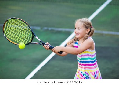Child playing tennis on outdoor court. Little girl with tennis racket and ball in sport club. Active exercise for kids. Summer activities for children. Training for young kid. Child learning to play