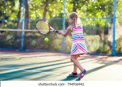 Child Playing Tennis On Outdoor Court. Little Girl With Tennis Racket And Ball In Sport Club. Active Exercise For Kids. Summer Activities For Children. Training For Young Kid. Child Learning To Play.