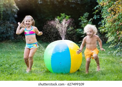 Child playing with toy ball garden sprinkler. Preschooler kid run and jump. Summer outdoor water fun in the backyard. Children play with hose watering flowers. Kids splash on sunny day