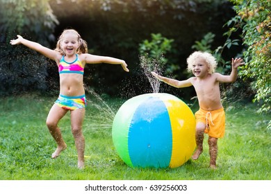 Child playing with toy ball garden sprinkler. Preschooler kid run and jump. Summer outdoor water fun in the backyard. Children play with hose watering flowers. Kids splash on sunny day.