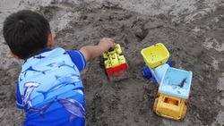 Child Playing With A Toy Construction Car In A Sand Pit.