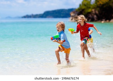 Child Playing With Toy Water Gun. Vacation And Beach Fun. Kids Run And Play With Plastic Pistol On Tropical Island Resort. Family Summer Holiday Activity At The Sea. Travel With Children. 