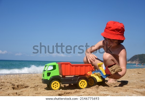 Child playing with a track and\
excavator in sand. Little boy play in sand on beach. Summer\
vacation