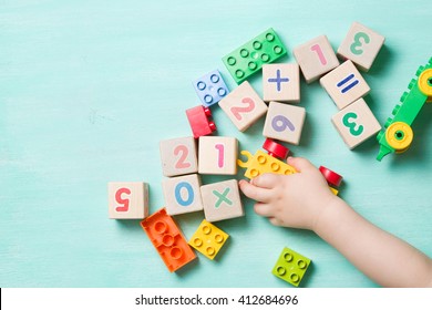 Child Playing With Wooden Cubes With Numbers And Colorful Toy Bricks On A Turquoise Wooden Background. Toddler Learning Numbers. Hand Of A Child Taking Toys.