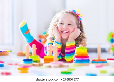 Child playing with wooden toys at preschool. Cute toddler girl having fun with toy blocks, building a tower at home or day care. Educational kids toy for nursery or kindergarten.