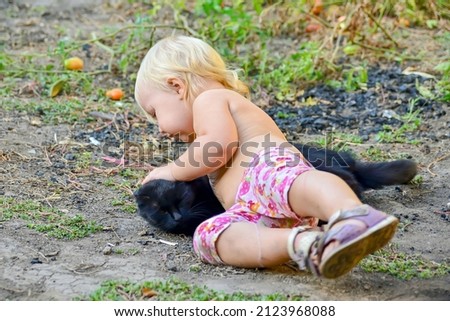 A child plays with a black cat in his yard on a summer evening.