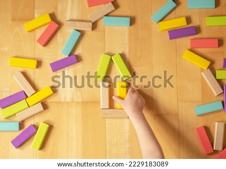 Child plays with colorful toy blocks on the ground in the flat. Educational game for children.