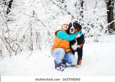 Child Plays With A Dog In The Winter In The Snow In The Backyard. Bernese Mountain Dog In A Family With Children, Walks With Kid. Dog Training And Childhood With Big Dog