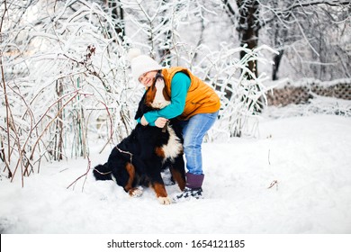 Child Plays With A Dog In The Winter In The Snow In The Backyard. Bernese Mountain Dog In A Family With Children, Walks With Kid. Dog Training And Childhood With Big Dog