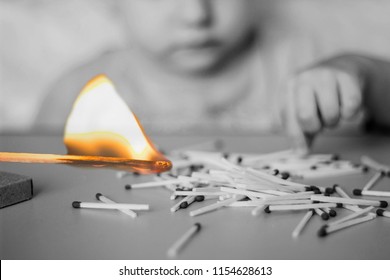 A Child Plays With Matches In The Foreground A Burning Match, A Child And Matches, A Fire, Dangerous, Black And White