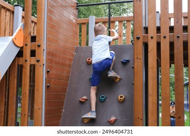 Child plays on an outdoor playground, climbing wooden wall. Little boy climbs wall in playground. Have happy and healthy childhood. - Powered by Shutterstock