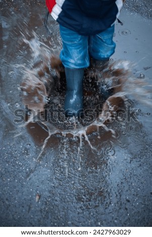 A child plays in a puddle - steps into a water with force and splashes fly away. Vertical image, motion blur, slight unsharpness.