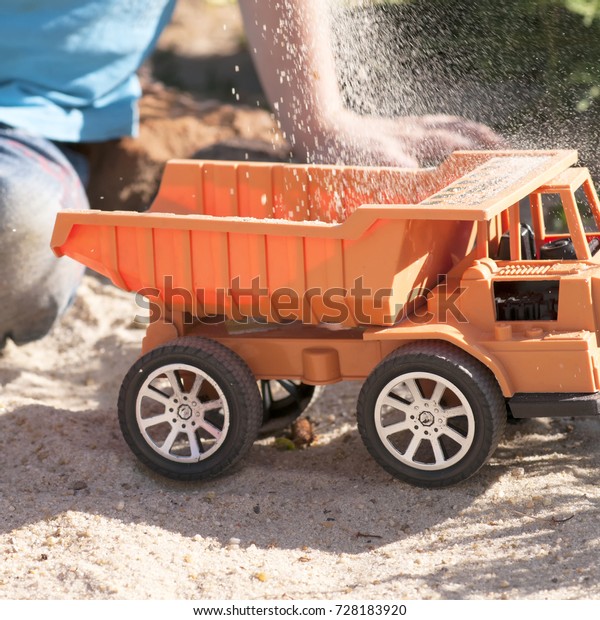A child plays in the sand with big toy cars, an\
excavator, a truck