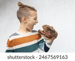 child plays with scary toy head of dinosaur, putting it on hand, scaring it with terrible grimace. Develop imagination and courage in children. boy studies ancient reptiles. Don