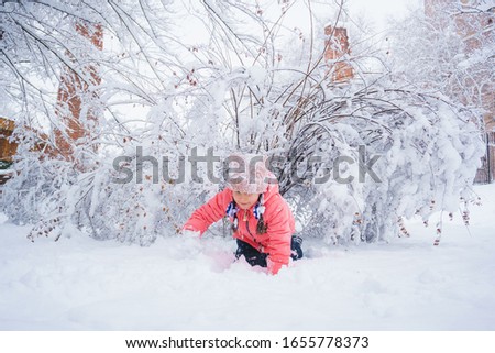 child plays in the snow in a park near a snowy bush