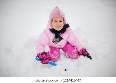 The child plays with snow in the winter. A little girl in a bright jacket and knitted hat, catches snowflakes in a winter park for Christmas. Children play and jump in the snow-covered garden.