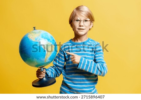 Child pointing at a globe, exploring Earth and global education concept on yellow background