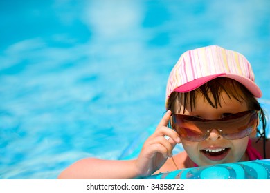Child in pool wearing sunglasses and cap laughing