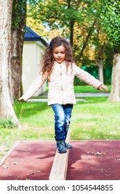 Child Is Practice Balancing In Playground, Girl Play Balance On Wooden Beam In Park