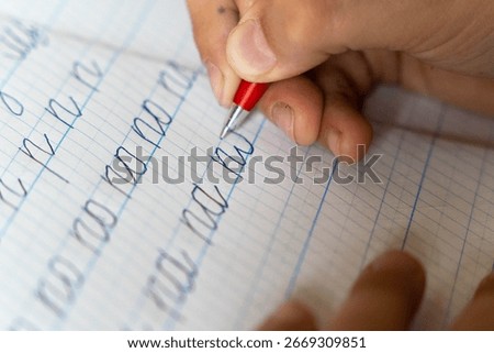 Child practicing cursive handwriting on squared paper with red pen