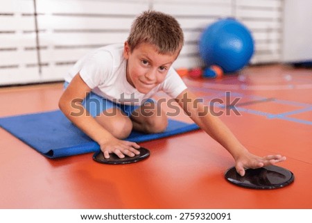 Child practicing a motoric coordination exercise with sliding discs to improve balance, upper body control and movement coordination during supervised functional training.