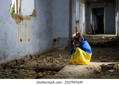 A child in prayer for peace. The child is wrapped in the Ukrainian flag. Ukrainian children during the war. A child in a bomb shelter. War in Ukraine. A child in a destroyed house. Russian aggression