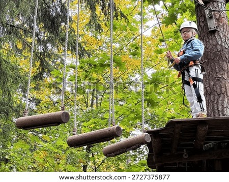 Child preparing for log obstacle course in autumn. Boy facing a log bridge obstacle in an autumn forest. Travel brochures and active lifestyle content.