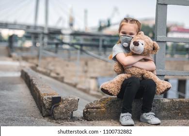 child in protective mask hugging teddy bear on street, air pollution concept