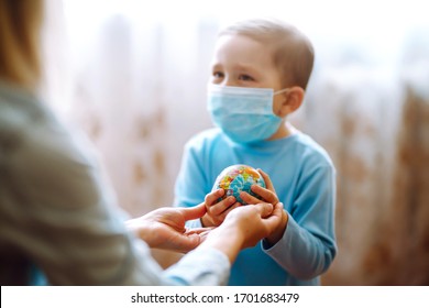 Child In Protective Sterile Medical Mask With Mother Holding A World Globe. Save Planet. The Concept Of Preventing The Spread Of The Epidemic Coronavirus.