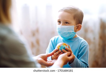 Child In Protective Sterile Medical Mask With Mother Holding A World Globe. Save Planet. The Concept Of Preventing The Spread Of The Epidemic Coronavirus.