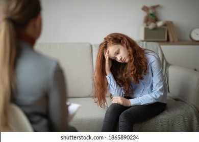 Child Psychologist. Worried sad teen girl having session with doctor or school teacher, grabbing head, sitting on the couch at office or home, thinking about her problems, feeling stress