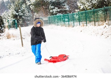 Child pulling red plastic sled. Winter fun