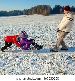 Child Pulls The Sleigh. Happy Family In Winter.  Dad Pulling Children On Sledge. Parent And Child Sledding.