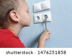 Child put fork in electric socket. Dangerous situation at home. Little boy playing with electrical outlet